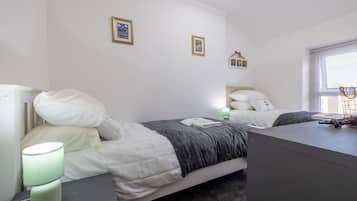 A bedroom with two beds, a bedside table with a lamp, and a dresser.