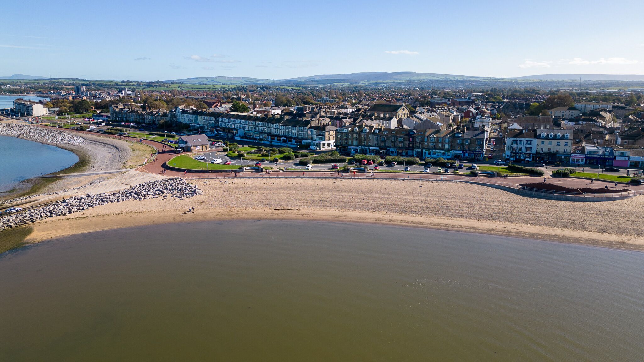 An aerial view of a coastal town with a sandy beach, residential buildings, and a large body of water.