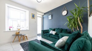 A modern living room with a dark blue accent wall, a green sofa set, a small round table with a basket, and a potted plant. - Morecambe Bay Cottage- Hot Tub/ Jacuzzi/sauna (Morecambe)