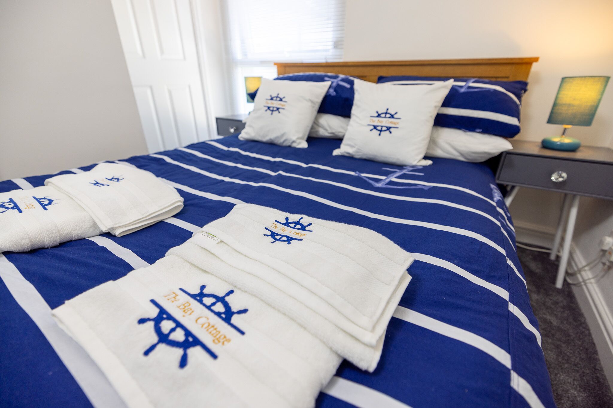 A neatly made bed with blue and white striped bedding, white towels with blue lettering, and matching pillows.