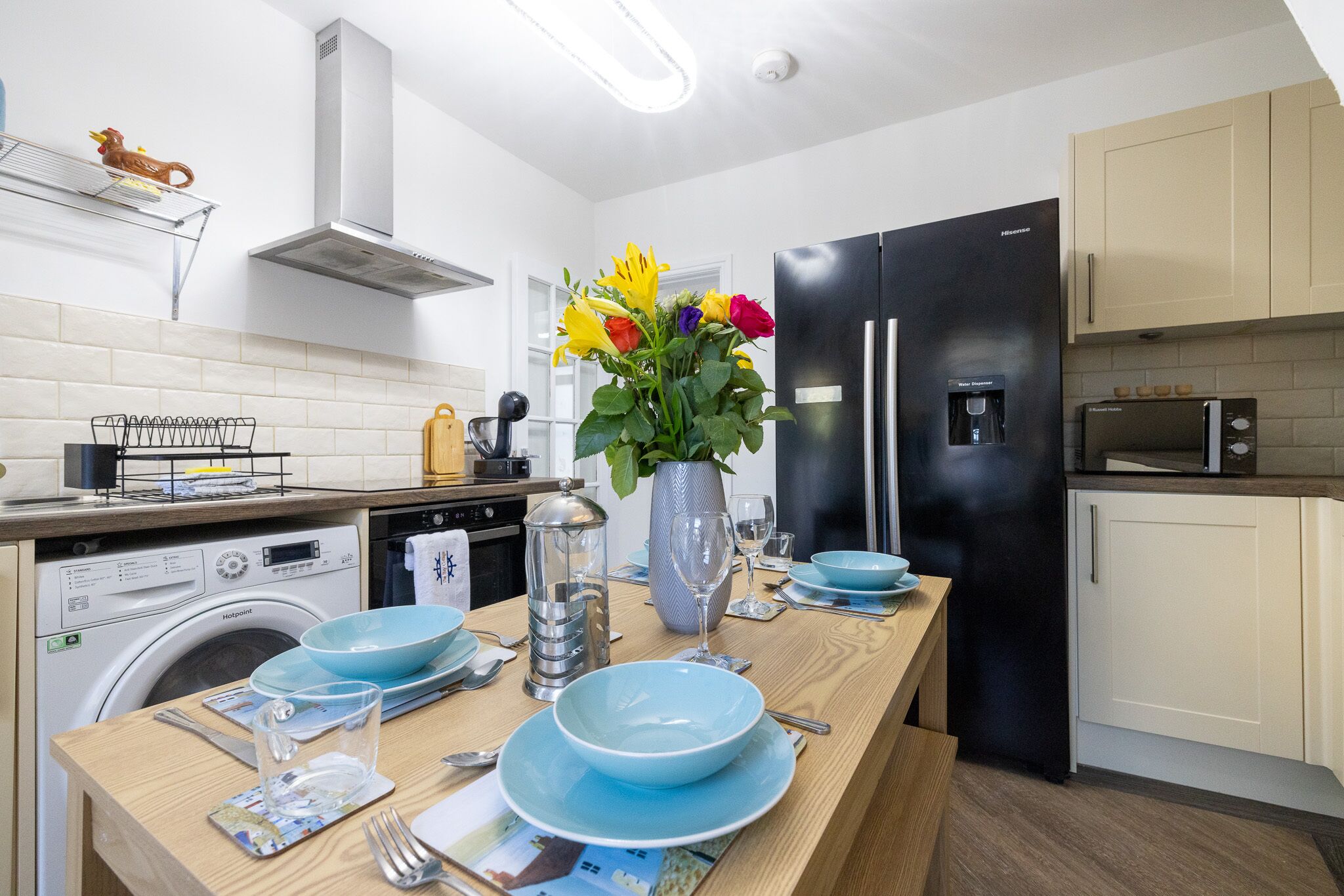 A modern kitchen with a central island, a black refrigerator, a microwave, and a washing machine.