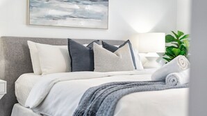 Un lit bien fait, avec une tête de lit grise, une literie blanche et grise, et un plaid gris.
