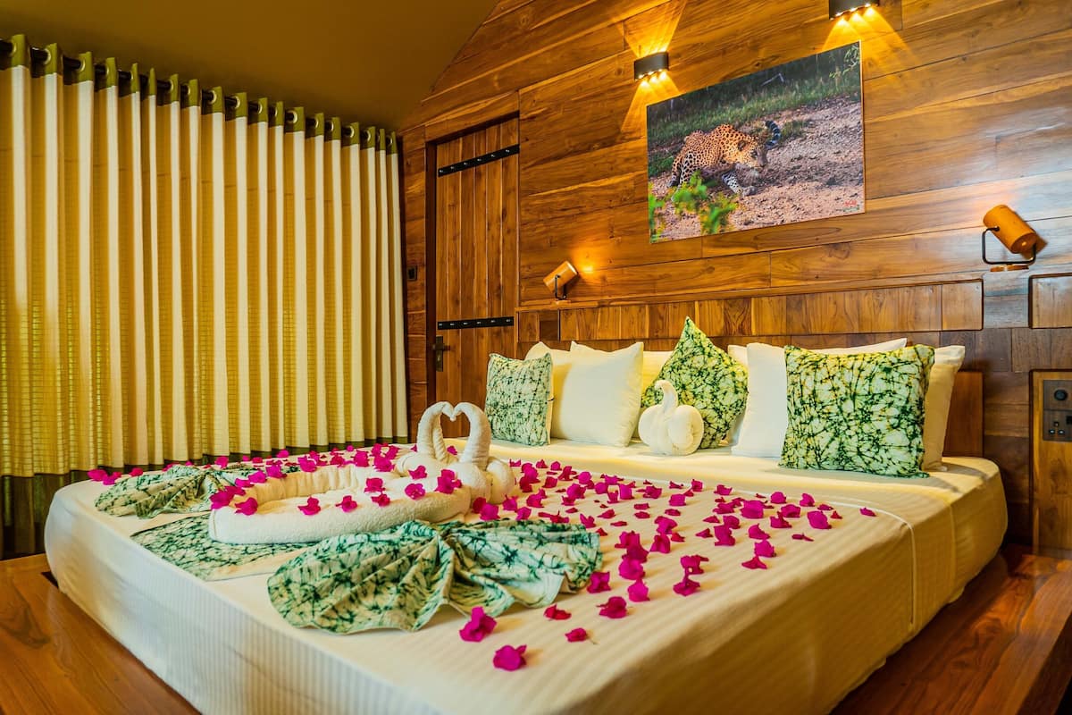 A well-appointed hotel room with a wooden wall, a large bed with floral bedding, and a painting of a leopard.