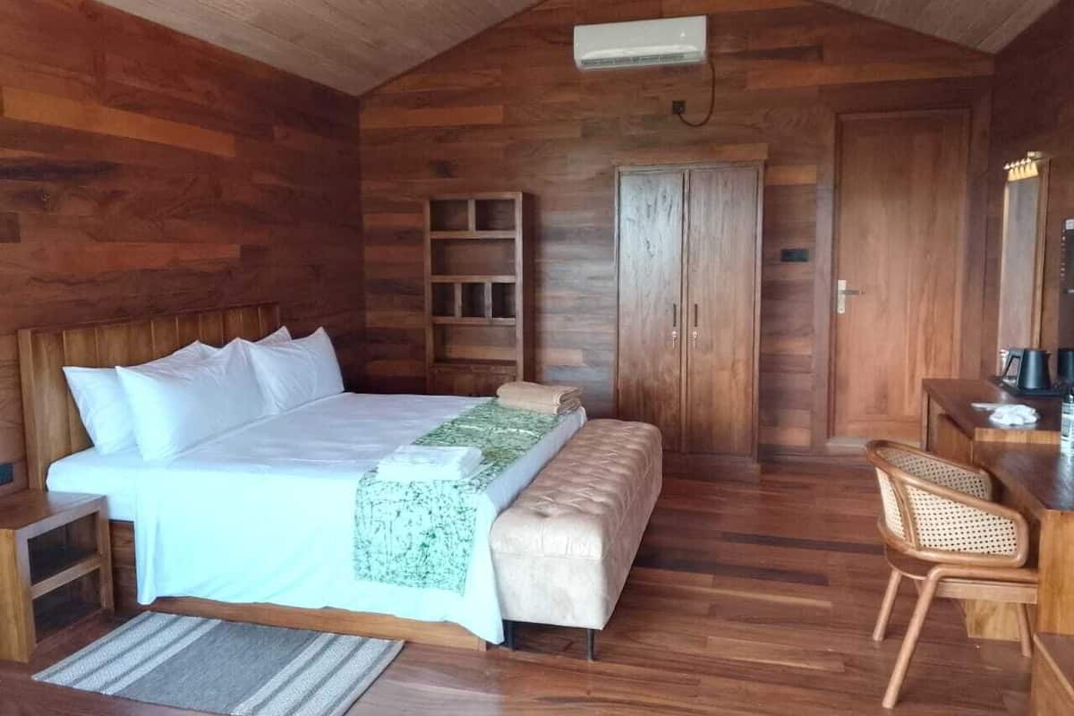 A wooden cabin-style bedroom with a bed, bench, bedside table, and a small desk with a chair.