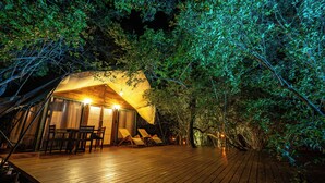 Alojamiento en tienda de campaña con terraza de madera, zona de estar e iluminación ambiental.