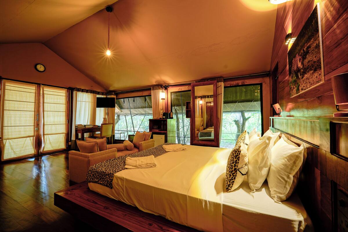 A spacious bedroom with a large bed, a sitting area with a sofa and chairs, and a TV.