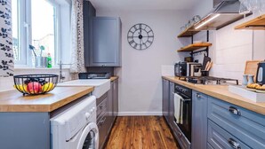 A modern kitchen with a wooden countertop, built-in appliances, and a large wall clock.