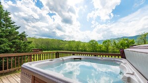 Een hottub op een houten terras met uitzicht op een bos en bergen.
