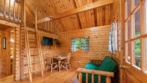 Een houten chalet interieur met een eethoek, een groene bank en een houten trap.