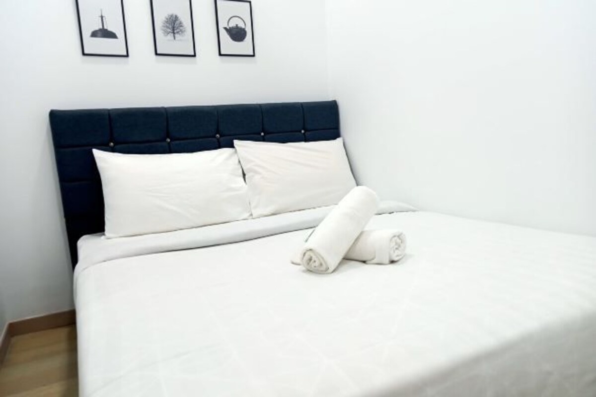 A neatly made bed with white linens and pillows, a dark blue upholstered headboard, and three framed pictures on the wall above.