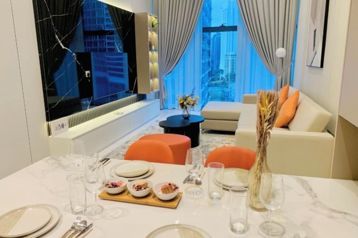 A modern living room with a dining area, a large TV, and a view of the cityscape.