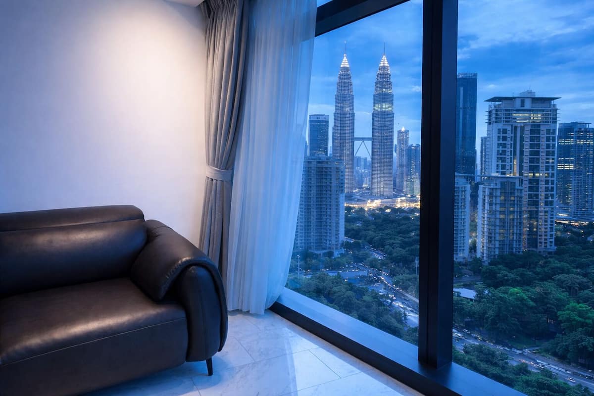 A modern room with a large window overlooking a cityscape, including the Petronas Towers.