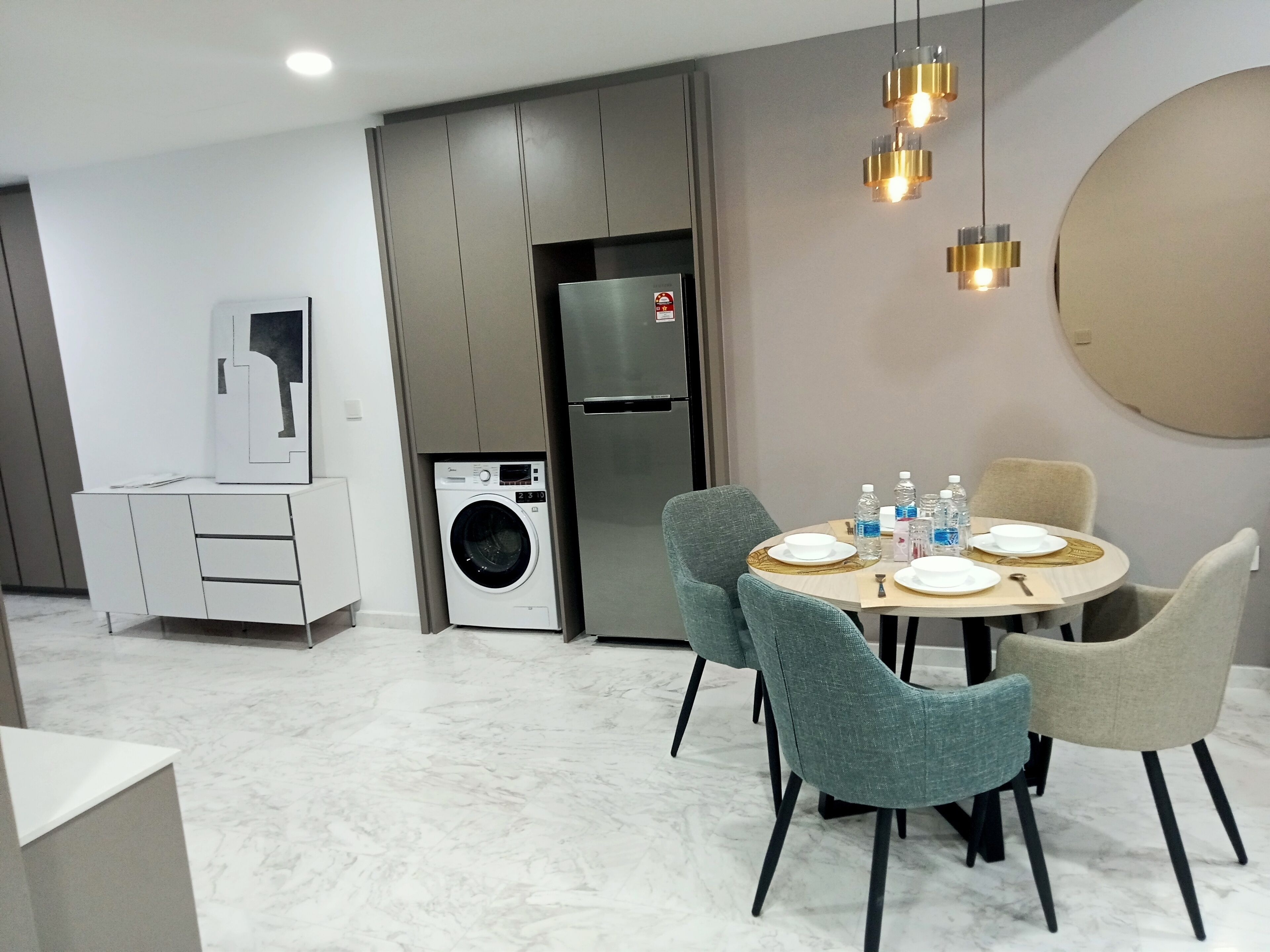 A modern kitchen with a built-in washing machine, a refrigerator, and a dining area with a round table and chairs.