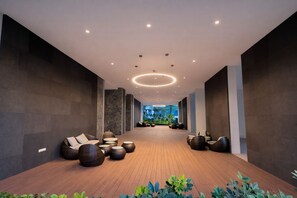 Een moderne lobby met een houten vloer, zithoeken en uitzicht op groen.