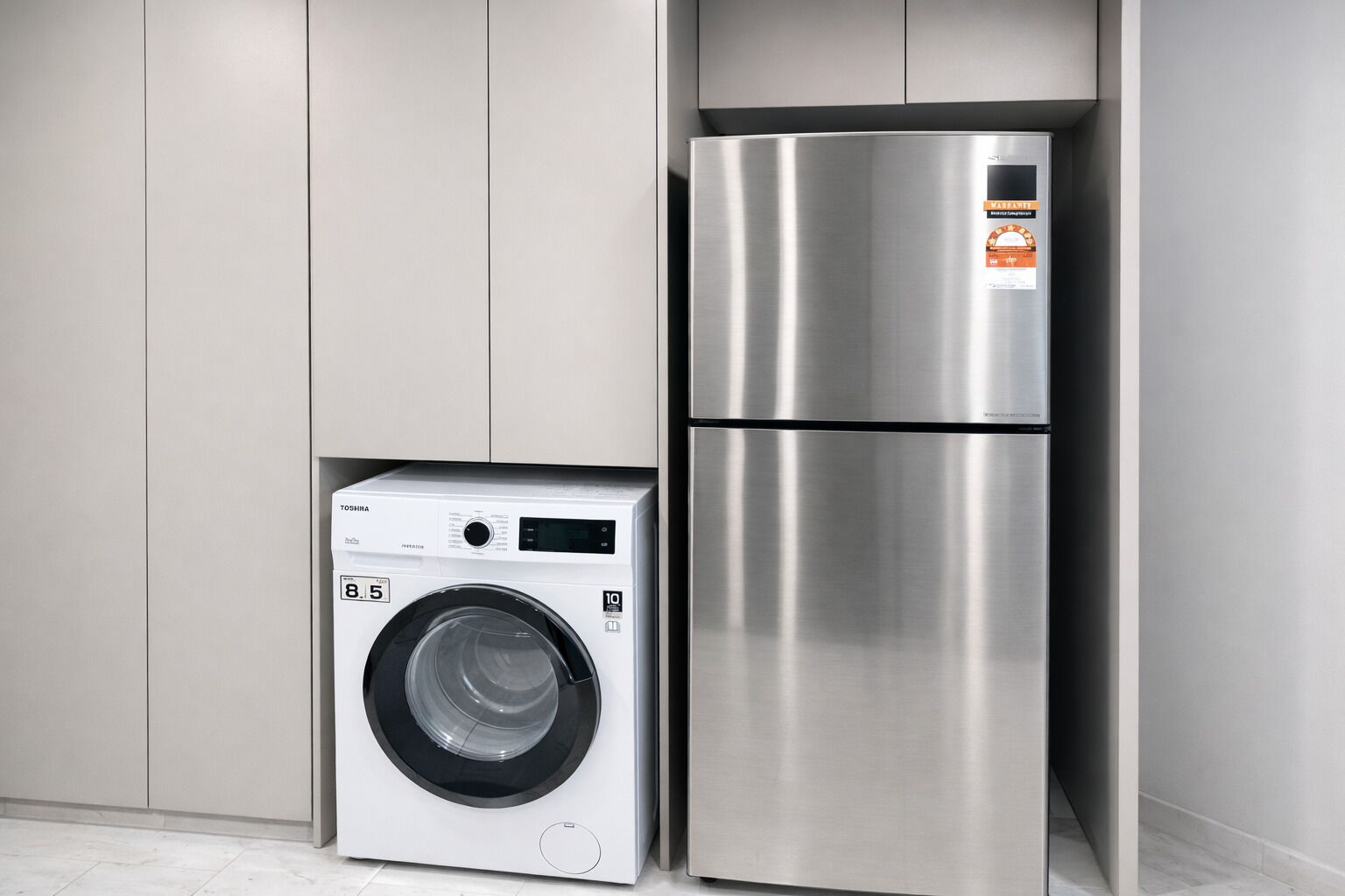 A compact kitchen with a stainless steel refrigerator and a front-loading washing machine.