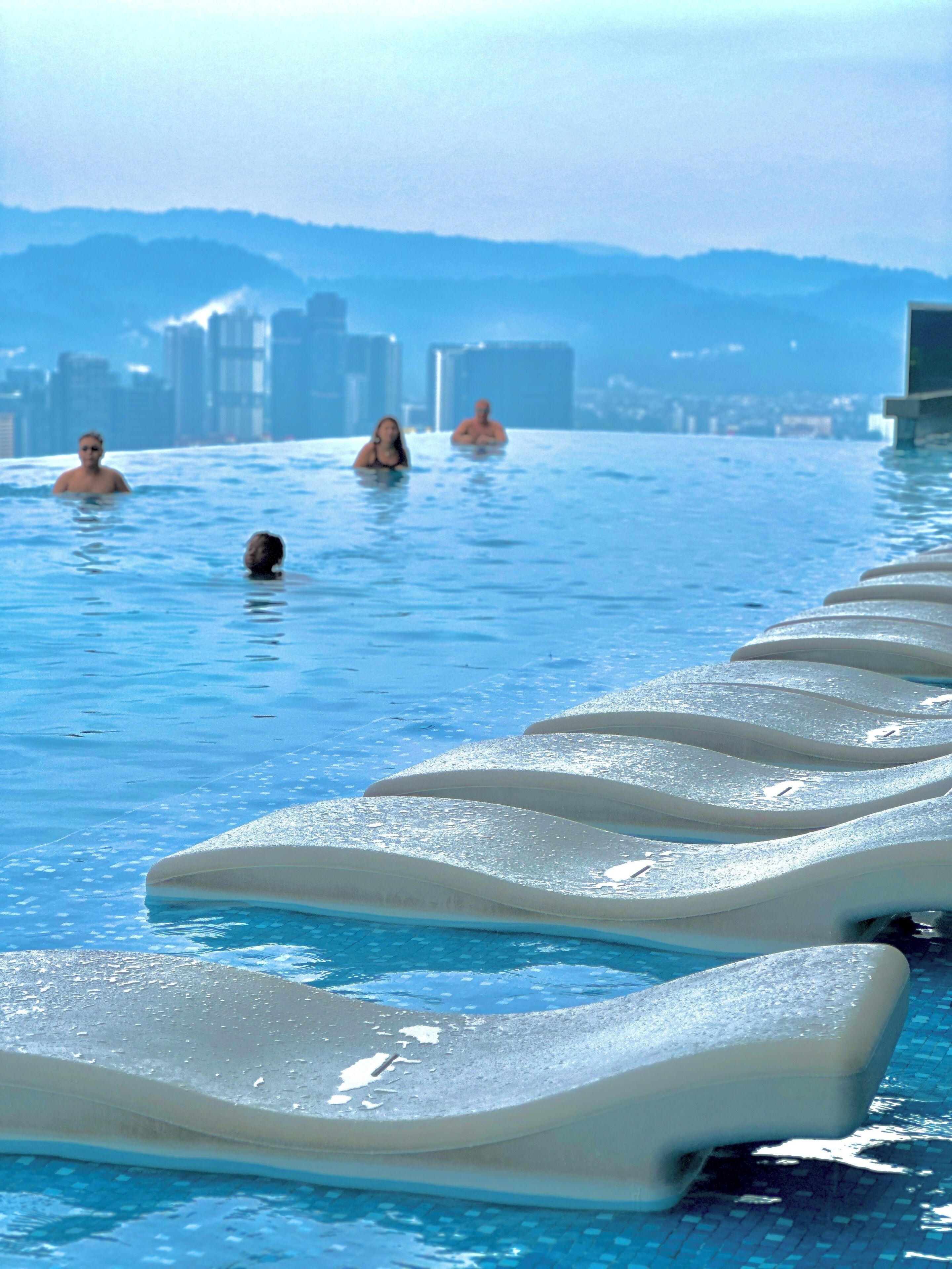 A swimming pool with lounge chairs and people in the water.