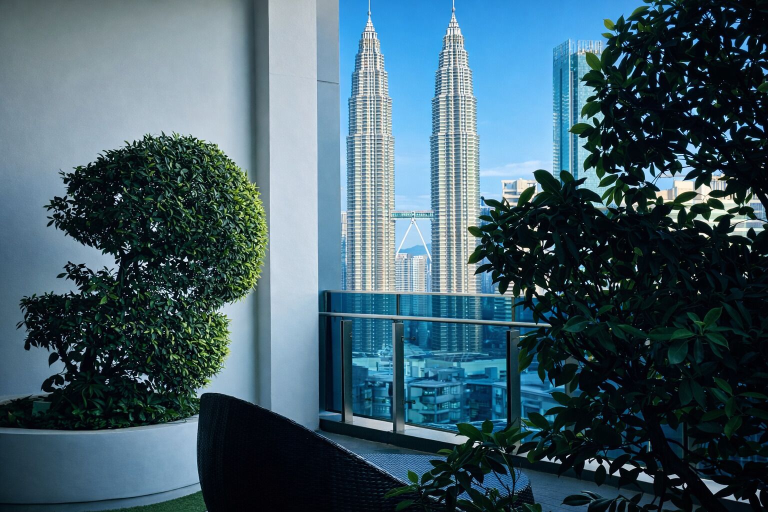 A balcony with a view of the Petronas Towers, a potted plant, and a wicker chair.