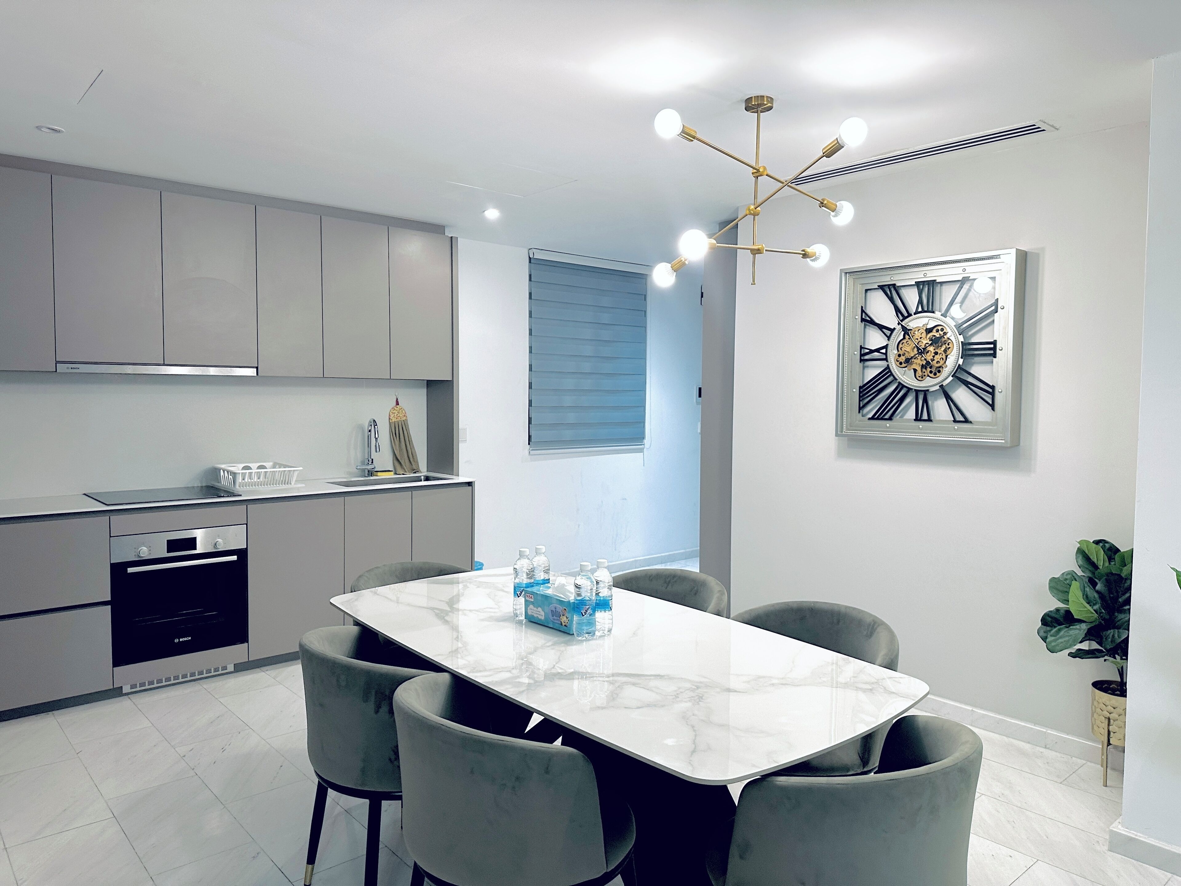 A modern kitchen with grey cabinets, a Bosch oven, and a marble dining table with four grey chairs.