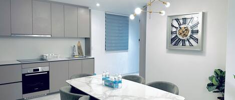 A modern kitchen with grey cabinets, a Bosch oven, and a marble dining table with four grey chairs.