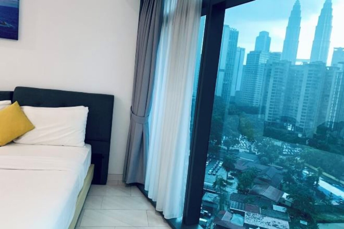 A bedroom with a bed, curtains, and a large window with a cityscape view.