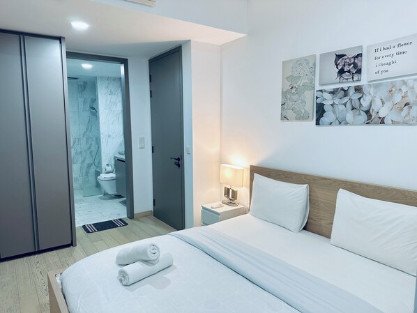 A hotel room with a bed, a nightstand, a wall-mounted lamp, and a door leading to a bathroom.