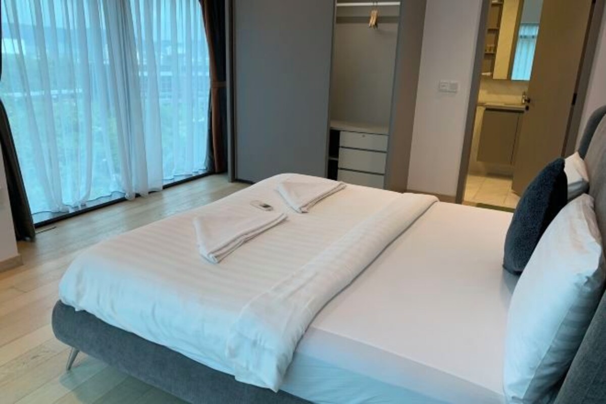 A modern bedroom with a large bed, a walk-in closet, and a bathroom visible through an open door.