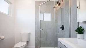 Un bany modern amb vàter, dutxa envidriada i un lavabo blanc amb mirall.