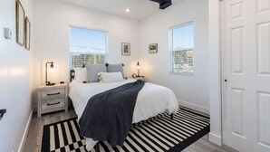Une chambre à coucher avec un lit, des tables de chevet, un tapis rayé noir et blanc et deux fenêtres.