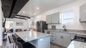 Une cuisine moderne dotée de plans de travail en granit, d’appareils électroménagers en acier inoxydable et d’un îlot central avec des tabourets de bar.