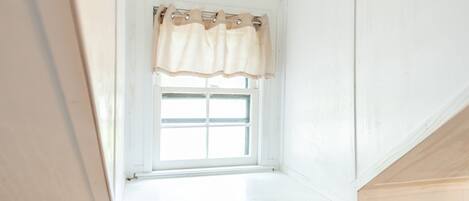 Una pequeña ventana de tejado con exterior blanco y cortina color beige.