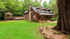 Une cabane rustique avec une cheminée en pierre, une terrasse en bois et un drapeau américain.