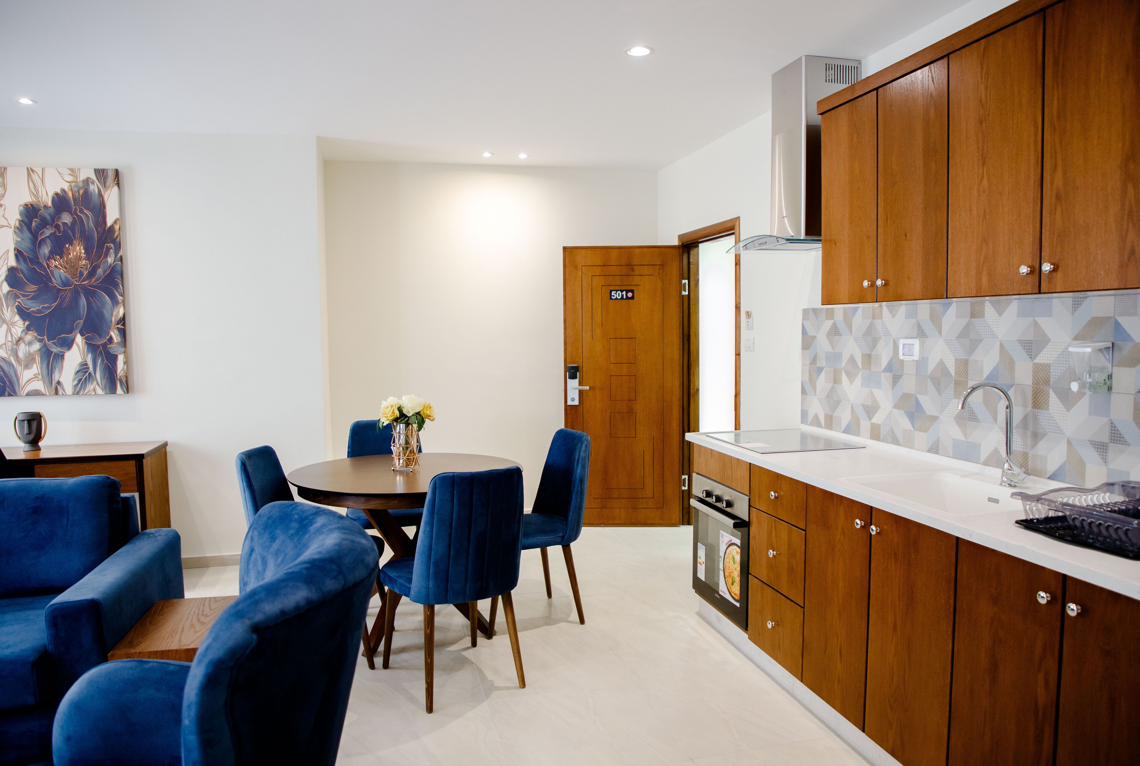 Una cocina moderna con armarios de madera, encimera blanca y zona de comedor con sillas azules y una mesa redonda.