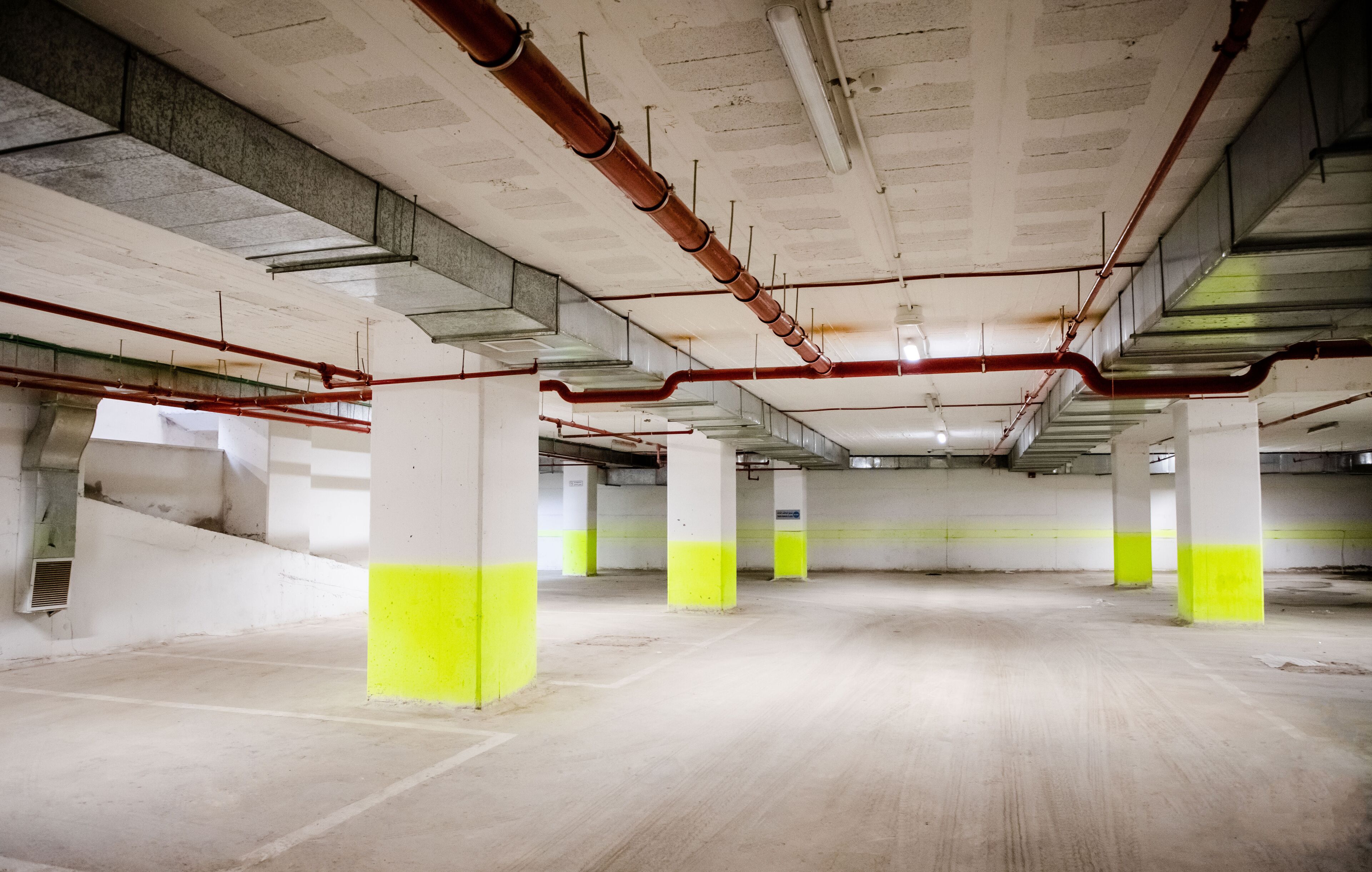 An empty parking garage with concrete pillars and exposed pipes.