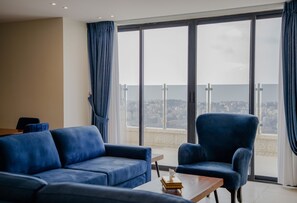 A modern living room with a blue sofa and armchair, a wooden coffee table, and large windows offering a city view. - Al-Istiklal Suites (Ramallah)