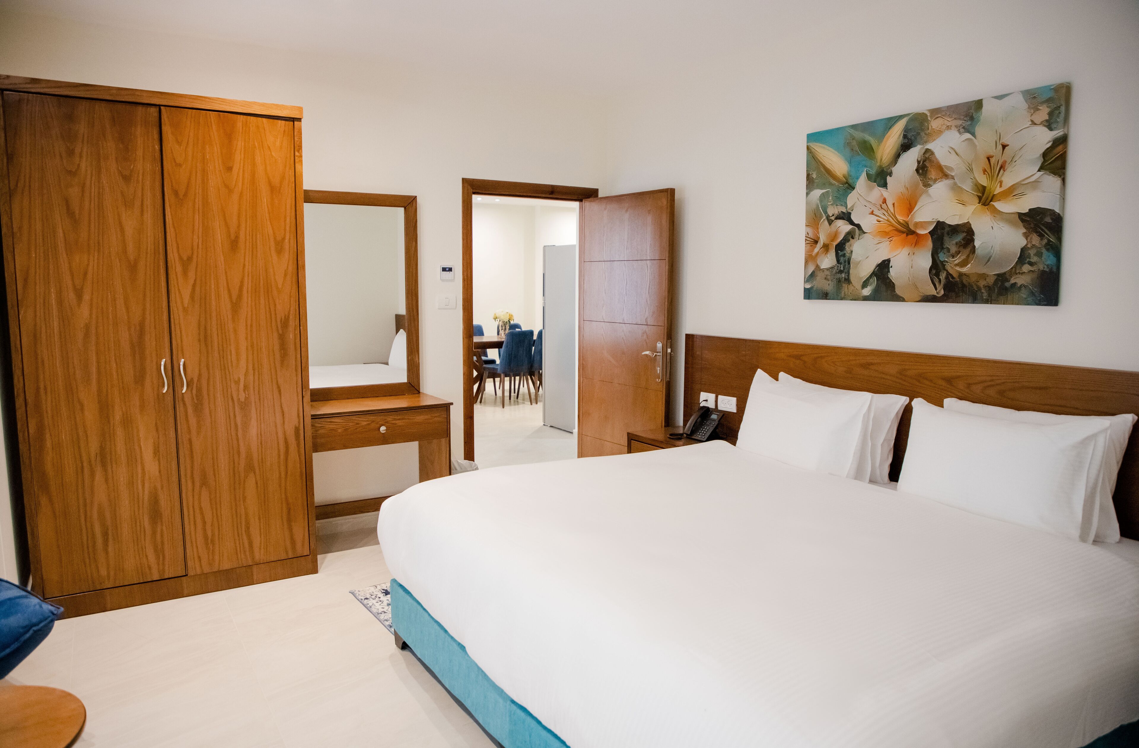 A hotel room with a large bed, wooden wardrobe, a bedside table, and a painting on the wall.