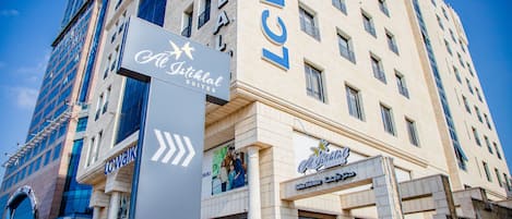 A hotel with a sign for 'Al Islah Suites' and 'LC Walkal' on the facade.