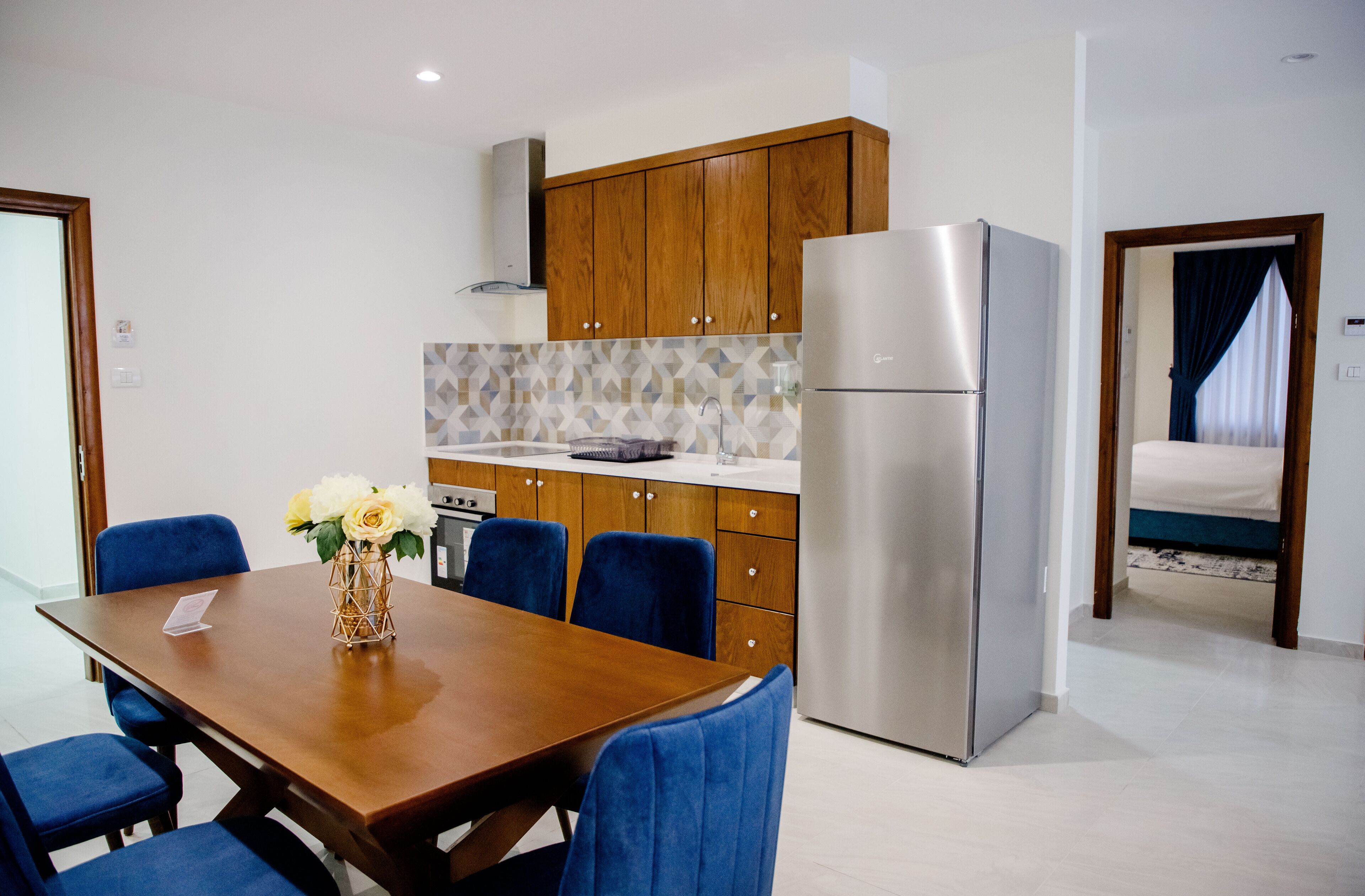 Een moderne keuken met houten kastjes, een roestvrijstalen koelkast en een eethoek met een houten tafel en blauwe stoelen.