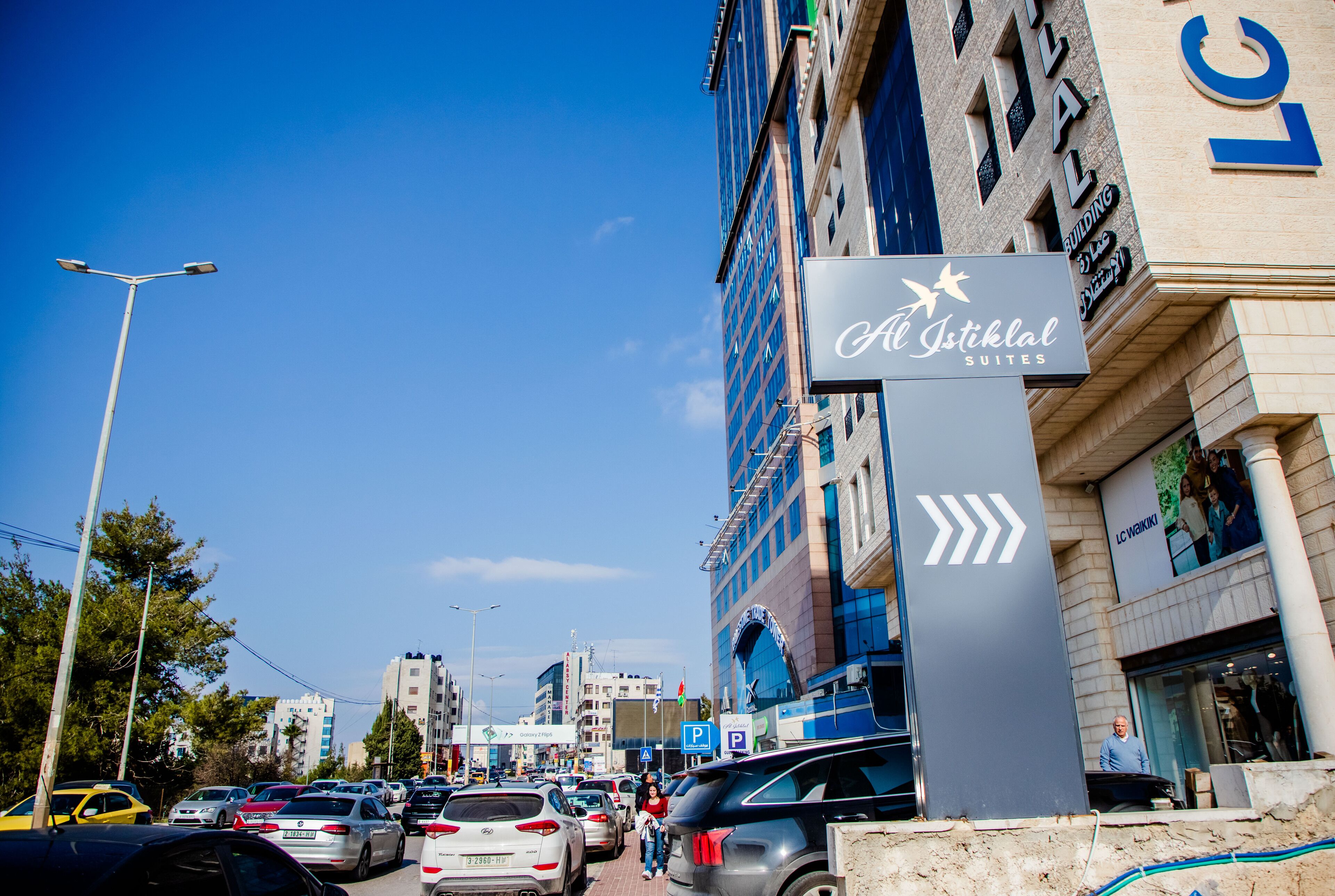 Letrero de hotel con un símbolo de estrella y el nombre 'Al Astiklal Suites' en un edificio alto.