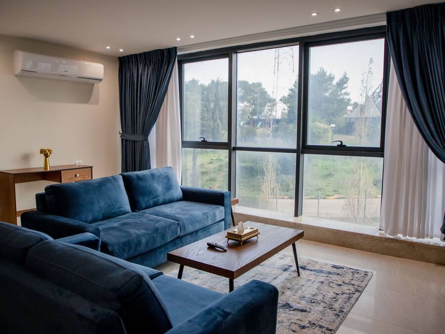 Ein modernes Wohnzimmer mit großem Fenster, einem blauen Sofagarnitur, einem Holztisch und einem kleinen Beistelltisch mit einer Vase.