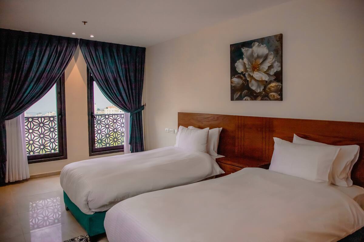 A hotel room with two beds, a wooden headboard, and a painting of flowers on the wall.
