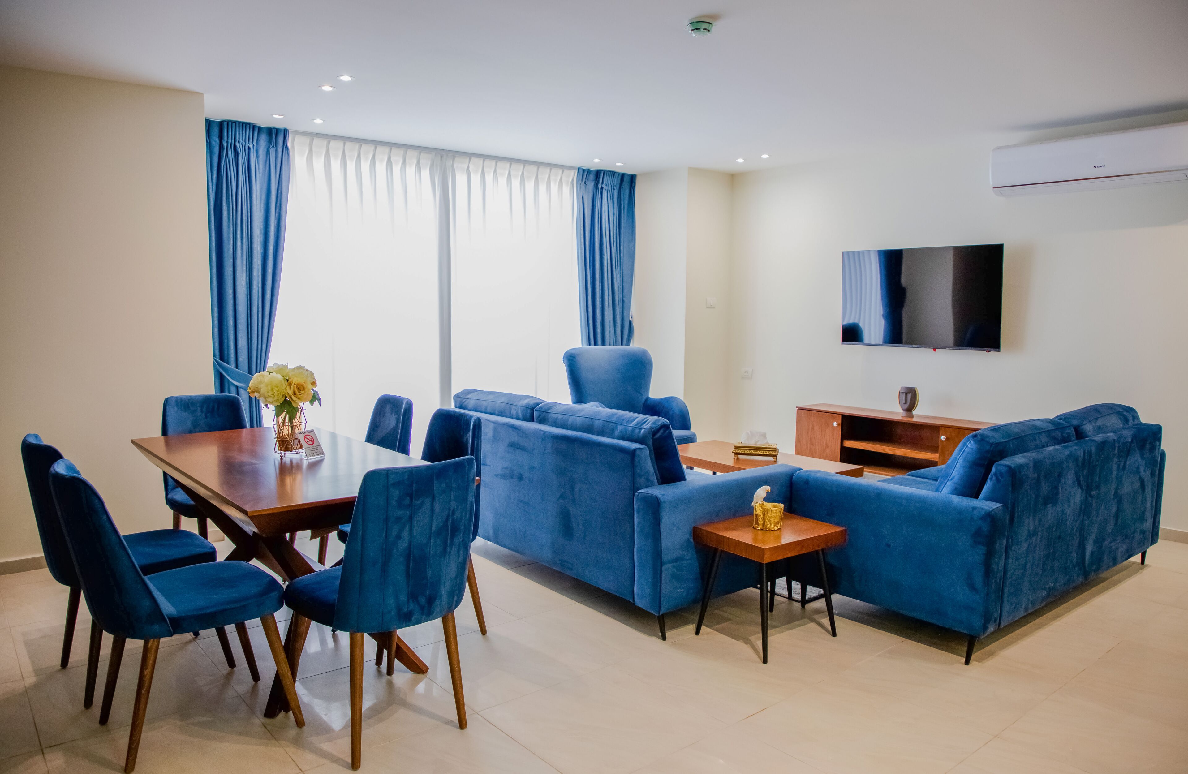 A modern living room with a dining table, blue sofas, and a TV.