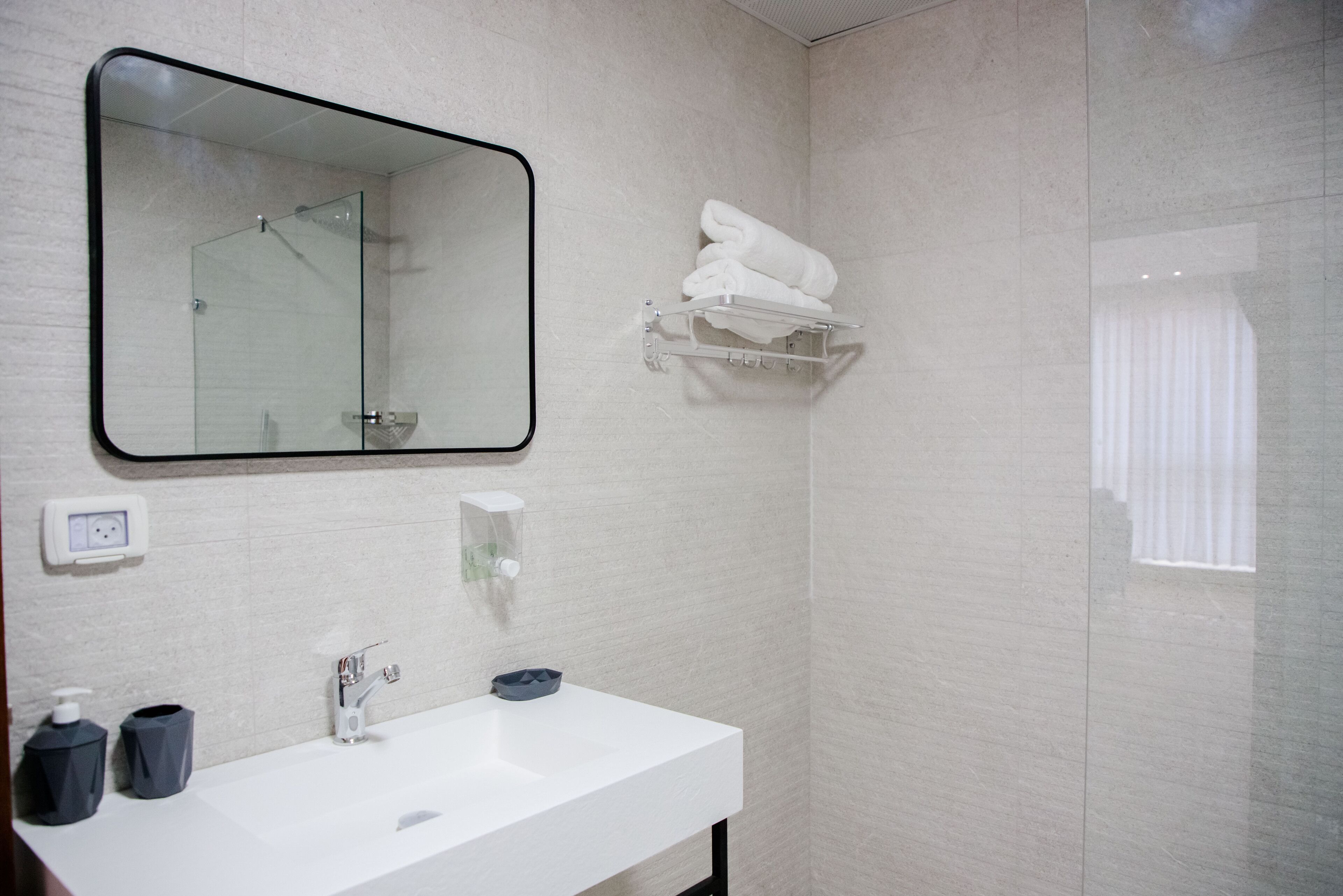 A modern bathroom with a large mirror, white sink, and a towel rack.