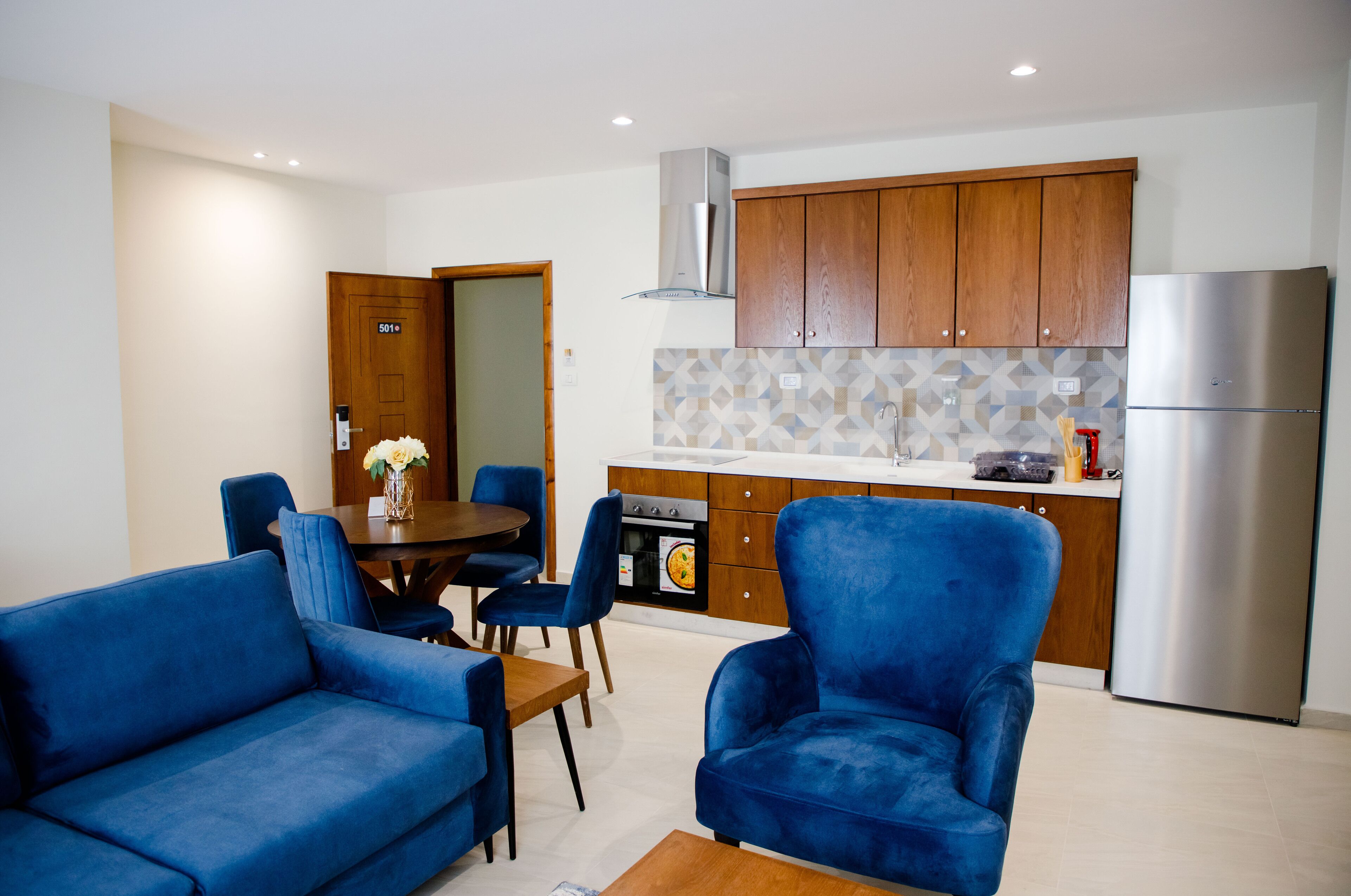 Una cocina moderna con armarios de madera, un refrigerador de acero inoxidable y una zona de comedor con sillas azules y una mesa.
