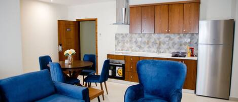 Una cocina moderna con armarios de madera, un refrigerador de acero inoxidable y una zona de comedor con sillas azules y una mesa.
