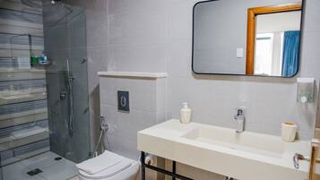 A modern bathroom with a glass shower enclosure, a white toilet, a sink with a mirror, and a towel rack.