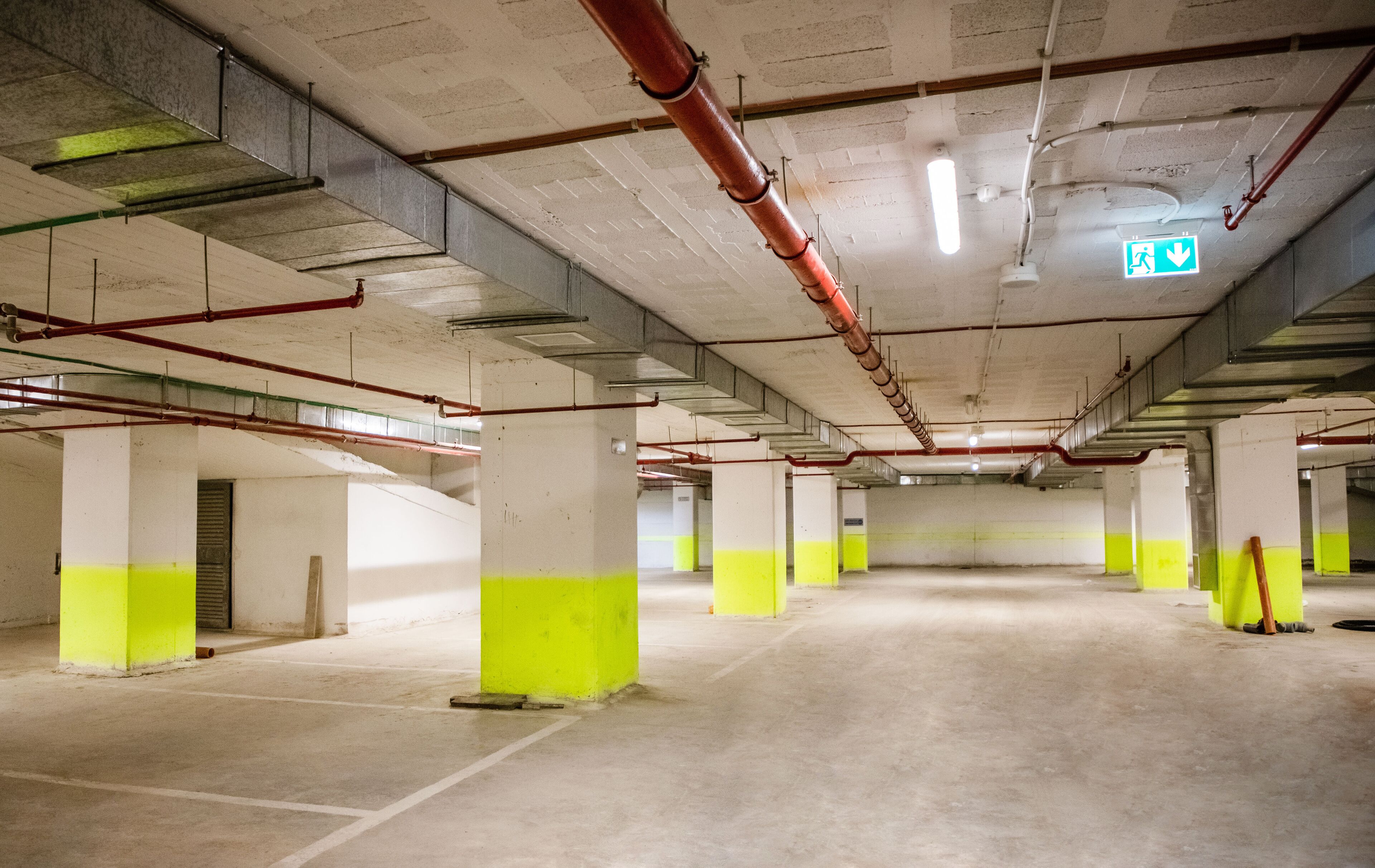 A multi-level parking garage with concrete pillars and overhead pipes.