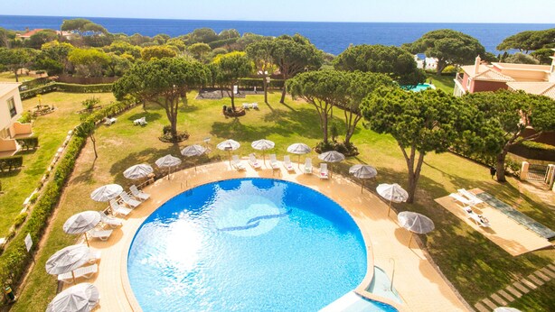 A large circular pool with a surrounding deck, lounge chairs, and umbrellas. - Cozy Apartment w/ Pool in Albufeira (Albufeira)