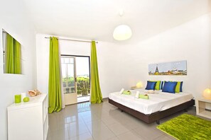 A modern hotel room with a bed, a desk, a chair, a window with curtains, a painting on the wall, and a balcony.
