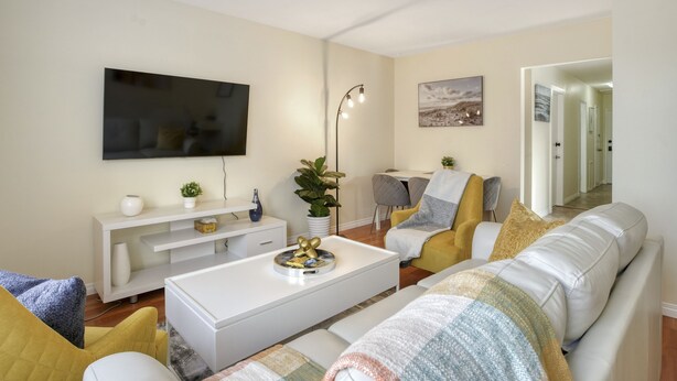 A modern living room with a white sofa, a coffee table, and a flat-screen TV mounted on the wall. - Fort Charm (Fort Saskatchewan)
