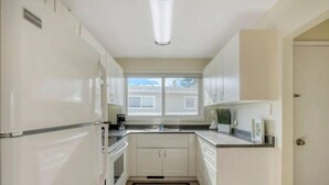 A compact kitchen with white cabinets, a built-in oven, and a window providing natural light. - Fort Charm (Fort Saskatchewan)
